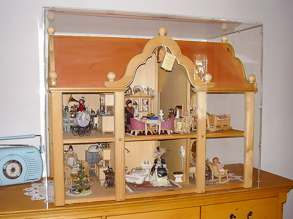 Sora-Maßhaube als Vitrine über einem zweistöckigen Puppenhaus mit Miniaturmöbeln und Figuren auf einer Holzkommode
