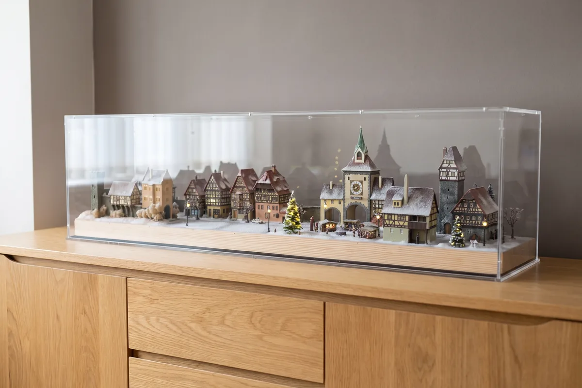 Beleuchtetes Miniaturdorf mit vielen Fachwerkhäusern unter einer langen maßgefertigten Acrylhaube